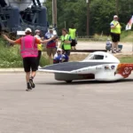 Student built solar car rounds a corner during the Electrek American Solar Challenge event on route.