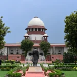 Front view of India's Supreme Court building framed by lush gardens beneath blue sky. on a sunny day