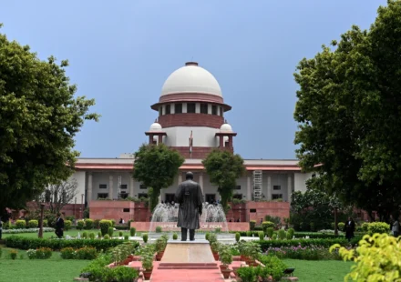 Front view of India's Supreme Court building framed by lush gardens beneath blue sky. on a sunny day
