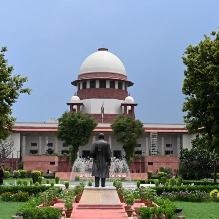 Front view of India's Supreme Court building framed by lush gardens beneath blue sky. on a sunny day