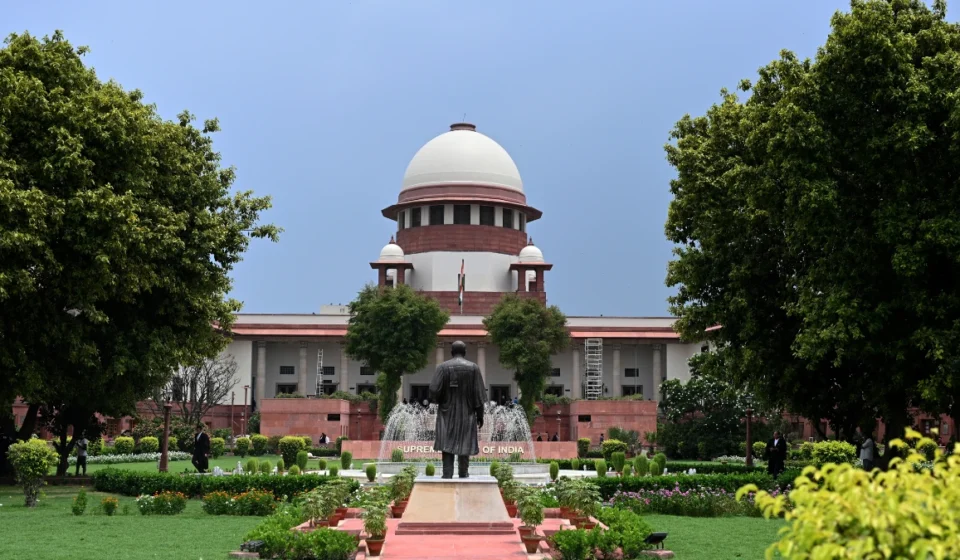 Front view of India's Supreme Court building framed by lush gardens beneath blue sky. on a sunny day