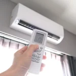 Hand holding a remote control to set a wall mounted air conditioner to 25 degrees Celsius