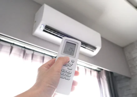 Hand holding a remote control to set a wall mounted air conditioner to 25 degrees Celsius