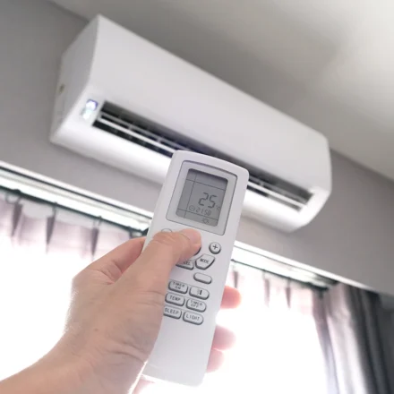 Hand holding a remote control to set a wall mounted air conditioner to 25 degrees Celsius
