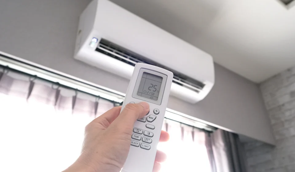 Hand holding a remote control to set a wall mounted air conditioner to 25 degrees Celsius