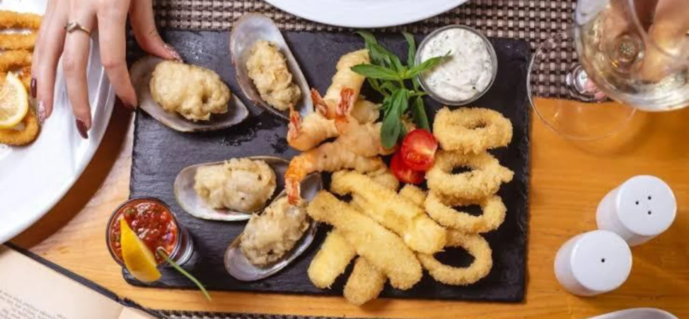 Assorted fried seafood platter with shrimp, calamari rings, and stuffed mussels on a slate board