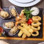 Assorted fried seafood platter with shrimp, calamari rings, and stuffed mussels on a slate board