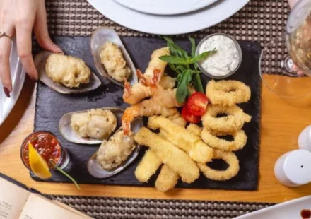 Assorted fried seafood platter with shrimp, calamari rings, and stuffed mussels on a slate board