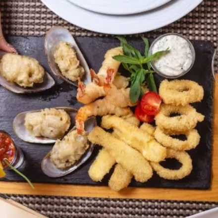 Assorted fried seafood platter with shrimp, calamari rings, and stuffed mussels on a slate board