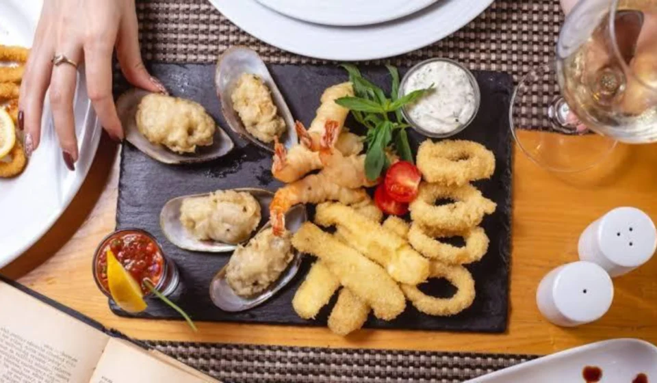 Assorted fried seafood platter with shrimp, calamari rings, and stuffed mussels on a slate board