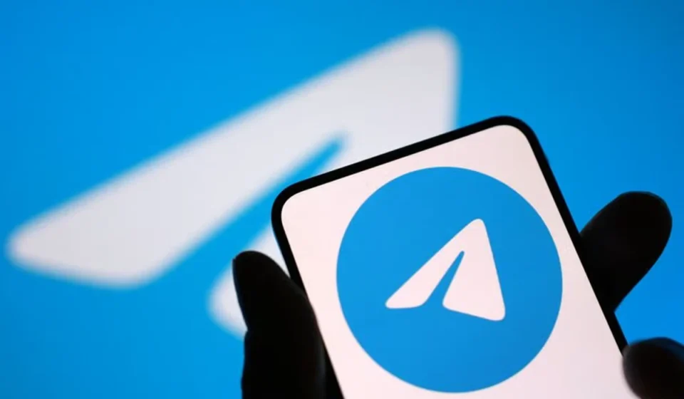 Hand holding smartphone displaying Telegram logo against blue background after App Store return news