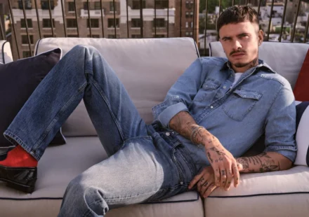 Model lounges on rooftop sofa wearing light blue denim shirt and jeans for Fall fashion campaign fit