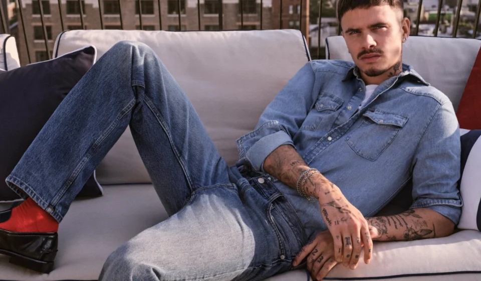 Tommy Hilfiger Debuts Global “Always Denim” Campaign with Romeo Beckham Model lounges on rooftop sofa wearing light blue denim shirt and jeans for Fall fashion campaign fit