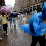 People in raincoats and umbrellas walk through flooded streets as a typhoon hits coastal China today.
