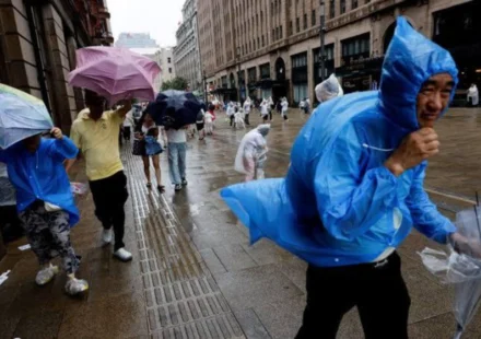 People in raincoats and umbrellas walk through flooded streets as a typhoon hits coastal China today.