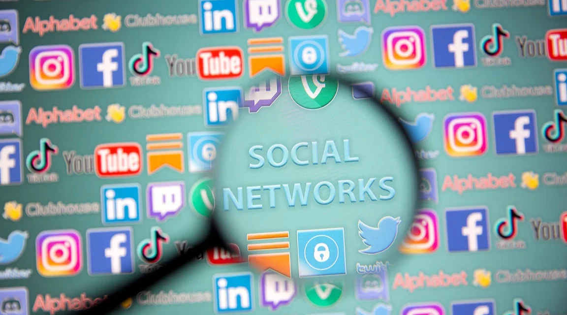 Magnifying glass over social media icons, highlighting concerns about youth online safety and harms.
