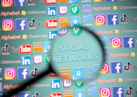 Magnifying glass over social media icons, highlighting concerns about youth online safety and harms.