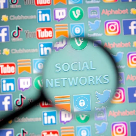 Magnifying glass over social media icons, highlighting concerns about youth online safety and harms.