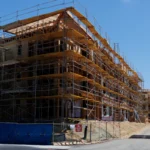 Construction workers walk past a multi story residential building under construction with scaffolding.