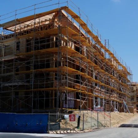 Construction workers walk past a multi story residential building under construction with scaffolding.
