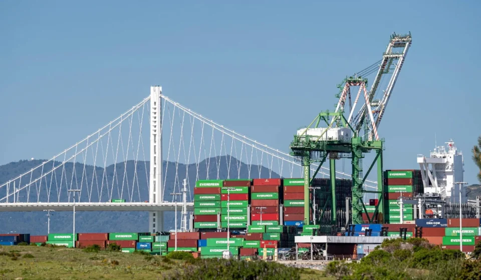 US Drafts Import Bans on Chinese Data Center Infrastructure Cargo containers and cranes at a busy US port beneath a suspension bridge reflecting global trade.