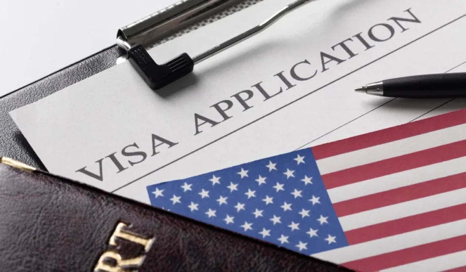 US Expands Social Media Vetting for Foreign Journalist Visas US visa application form with American flag, passport, pen, papers showing journalist visa vetting.