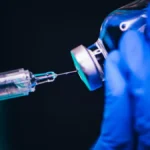 Scientist in blue gloves prepares a syringe with a vaccine vial for respiratory disease research study use.