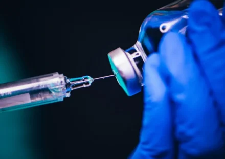 Scientist in blue gloves prepares a syringe with a vaccine vial for respiratory disease research study use.