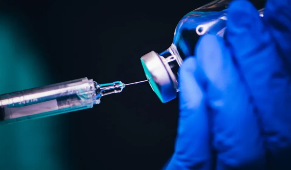 Scientist in blue gloves prepares a syringe with a vaccine vial for respiratory disease research study use.